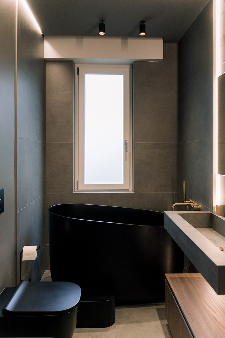 Bagno piccolo completato con rivestimento in pietra scura, vasca ovale nera e rubinetteria dorata