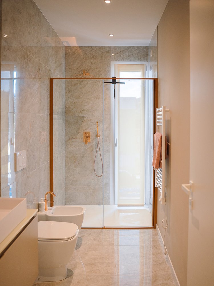 Bagno completato a Vicenza dopo la ristrutturazione: doccia in marmo con rubinetteria oro rosa e box doccia in vetro